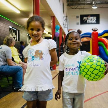 Two girls smiling indoors, one holding a green ball.