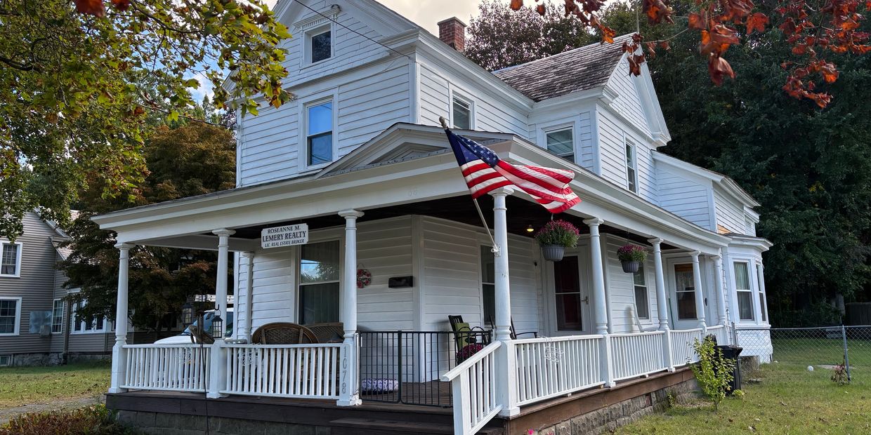 White two-story house with a front porch and an American flag.