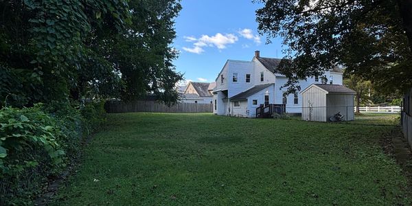 Green backyard with white house and shed under blue sky.