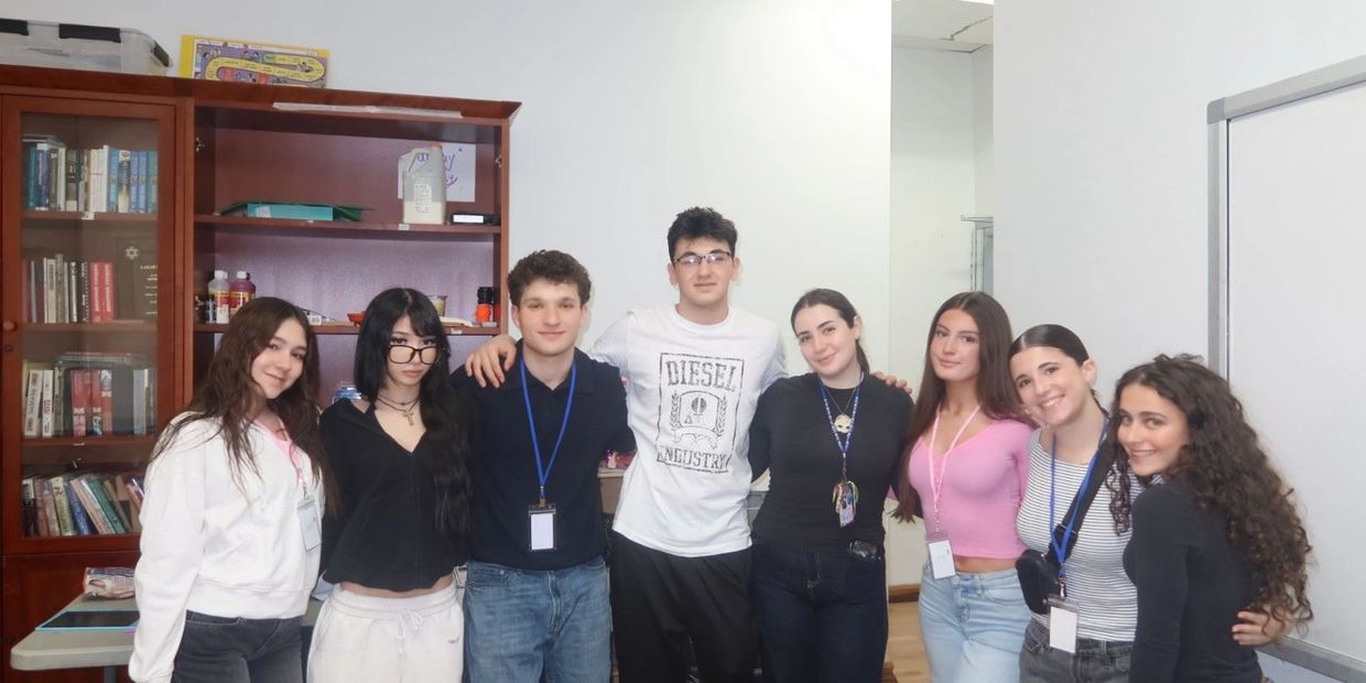 A group of eight young people posing and smiling indoors.