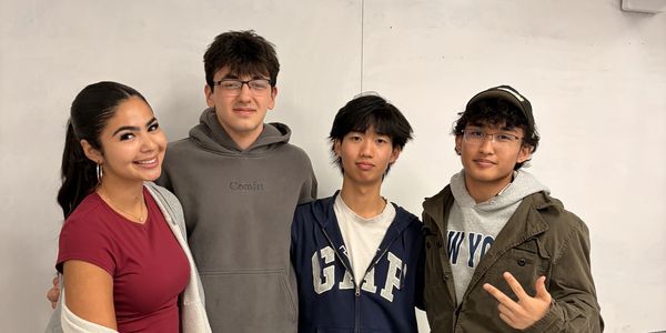 Four young adults posing together and smiling indoors.