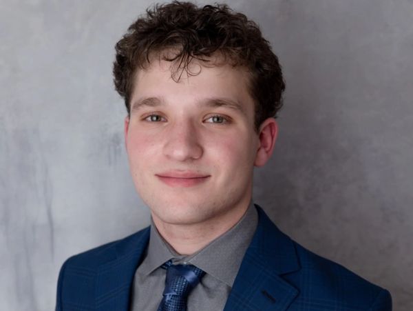 Young man in a blue suit and gray shirt smiling.