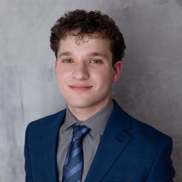 Young man in a blue suit and gray shirt smiling.