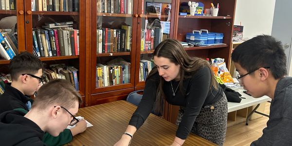 A teacher helps three students at a library table.