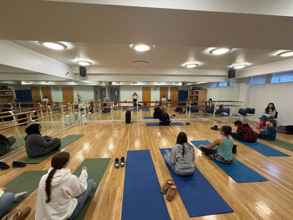 Group yoga session in a bright studio with wooden floors and mirrors.