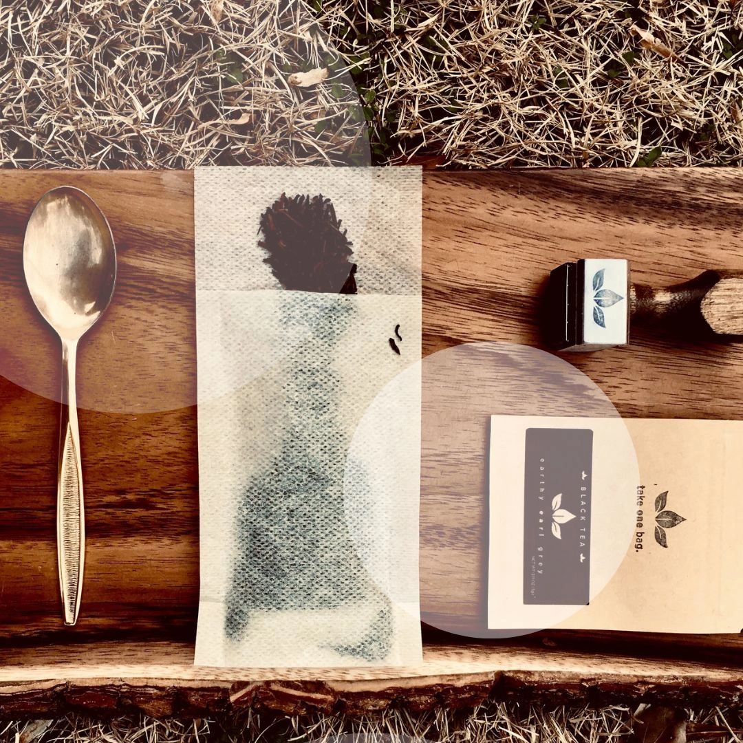 A wooden board holds a spoon, tea bag, and tea packaging outdoors.