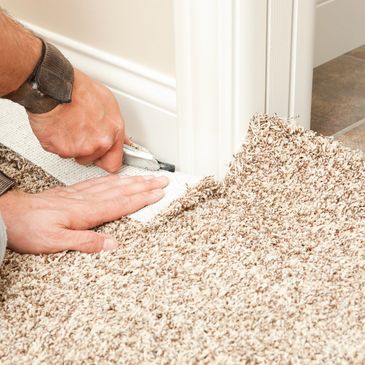 Hands installing carpet with a cutting tool.