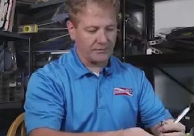 Man in blue polo shirt working with a tool indoors.