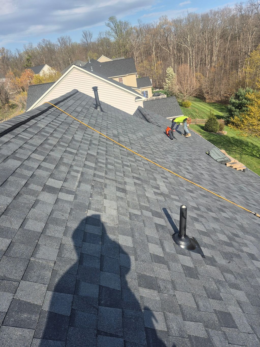 Two workers installing shingles on a residential roof on a clear day.