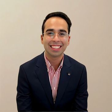 Smiling young man in glasses wearing a navy blazer and striped shirt.