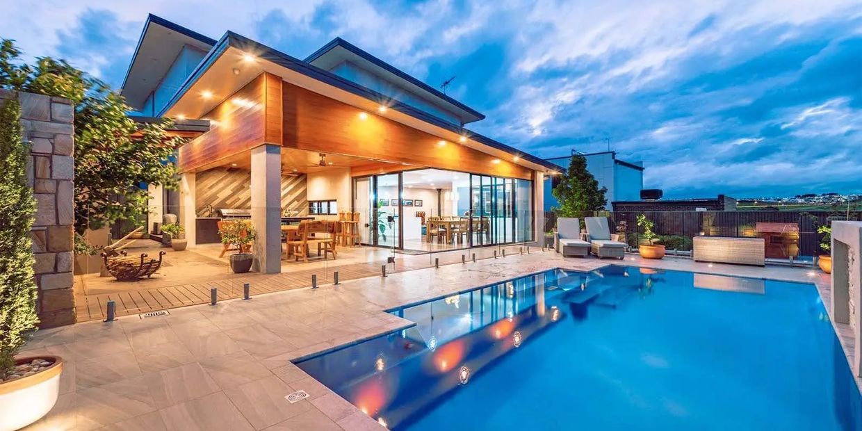 Modern house with an illuminated pool and outdoor seating at dusk.