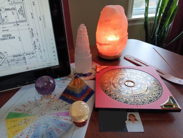 A feng shui setup with crystals, a salt lamp, and compass on a wooden table near a computer screen.