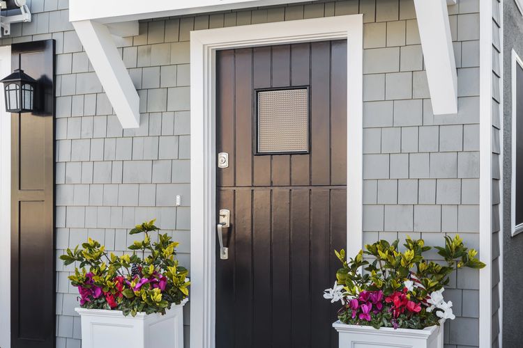 Modern black front door with white trim and colorful flower pots on each side.