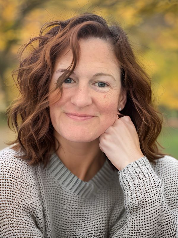 Smiling woman with curly hair in a cozy sweater outdoors in autumn.