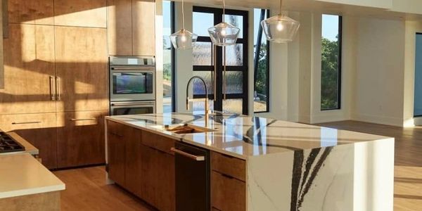 Modern kitchen with wooden cabinets and marble island under pendant lights.