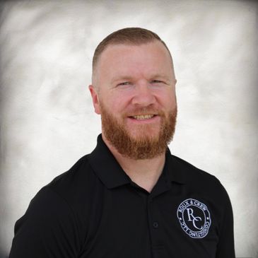 Smiling man with a red beard wearing a black polo shirt with a consulting logo.