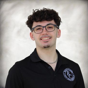 Young man with curly hair and glasses smiling in a black polo shirt.
