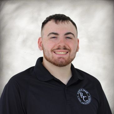 Smiling young man in a black polo shirt with a company logo.