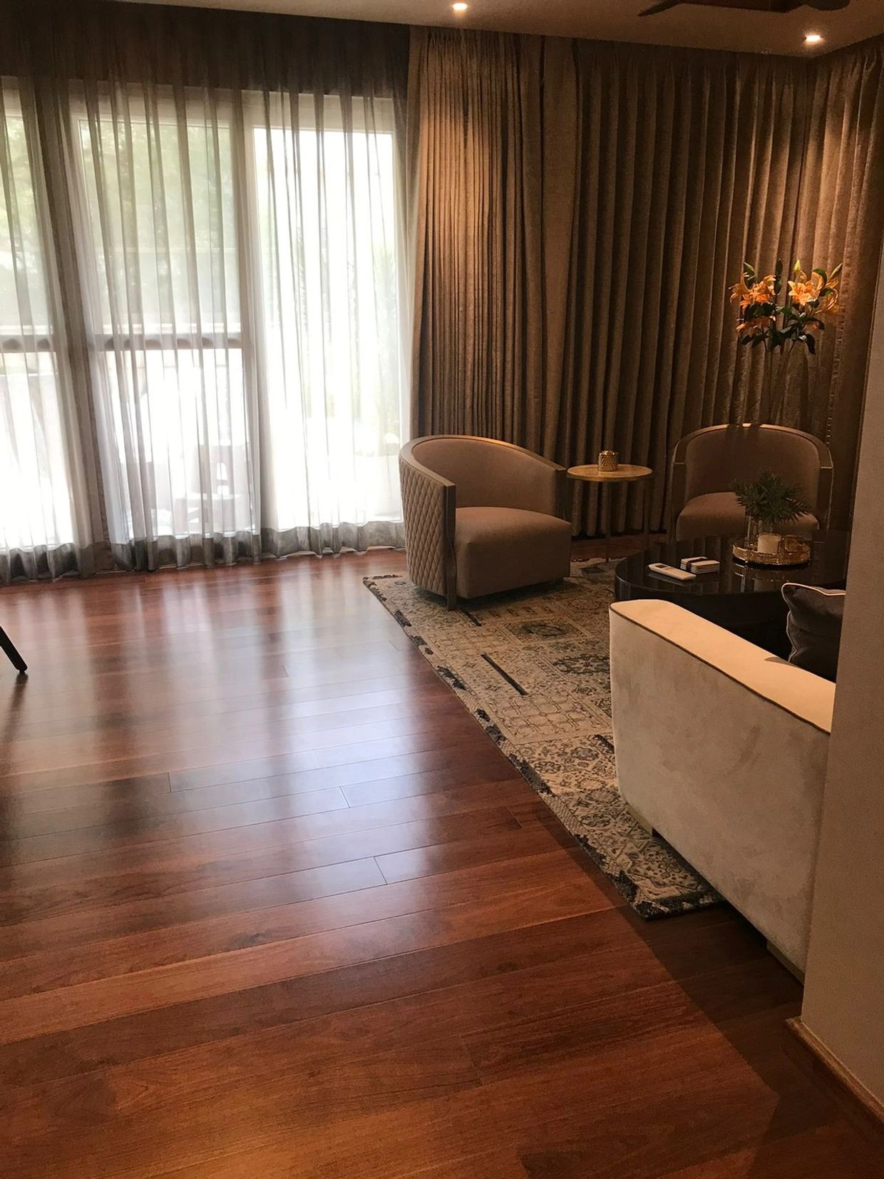 Cozy living room with wooden flooring and beige furniture near large windows.