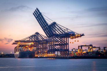 Cranes and cargo ship at a port during sunset.