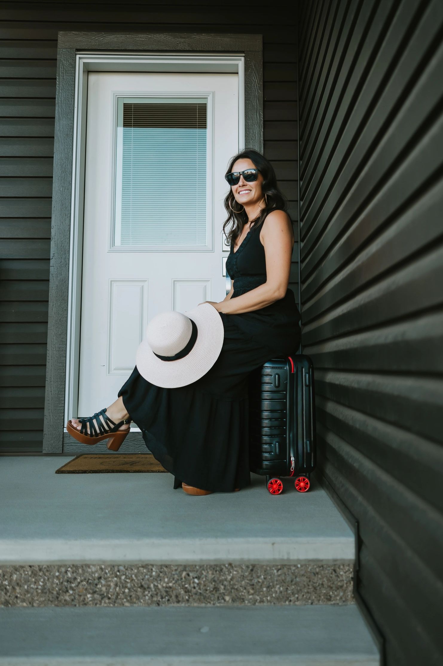 Annette Bruneau is sitting on her suitcase, holding a hat, ready to travel.