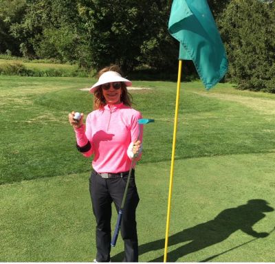 Woman golfer holding golf ball and putter near the hole flag on green.