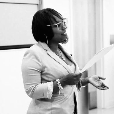 Woman speaking and holding a sheet of paper in a professional setting.