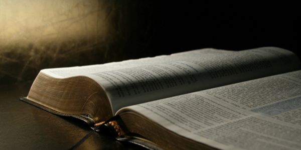 An open book illuminated by soft light on a dark surface.