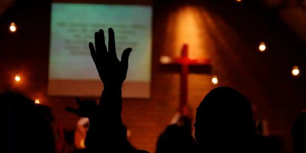 Silhouetted hand raised in worship inside a dimly lit church.
