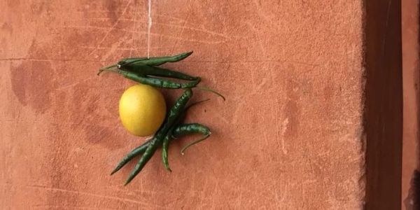 A lemon and green chilies forming a pattern on a textured wall.