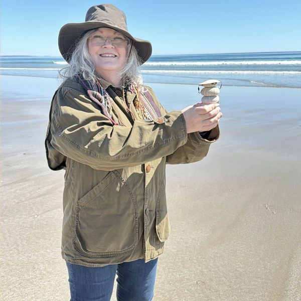 A woman on the beach holding a stack of balanced stones.