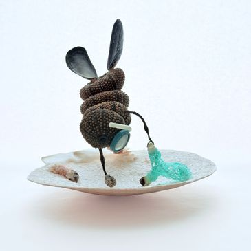 An artistic insect sculpture made with beads and fabric on a shell.