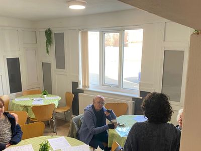A group of people sitting and talking around tables with papers in a cozy room.