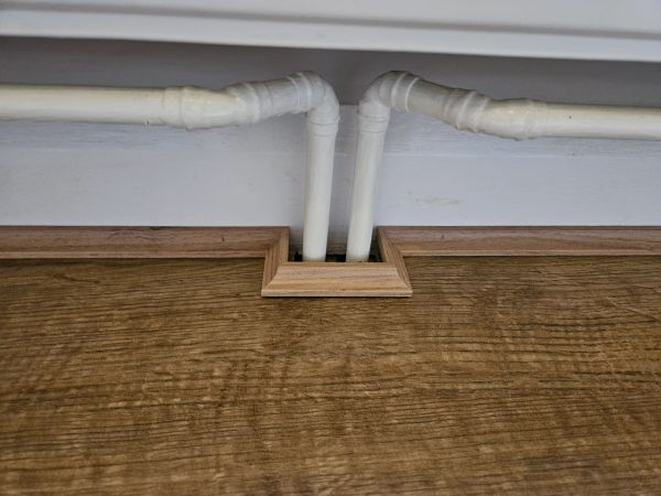 Wood panel with precise cut for white pipes.