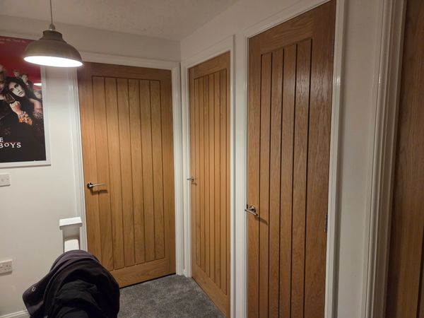 Three wooden doors in a hallway with a coat on a chair.