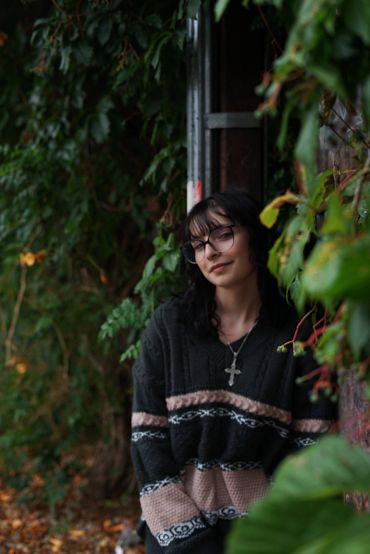 Woman leaning against wall with greenery around.