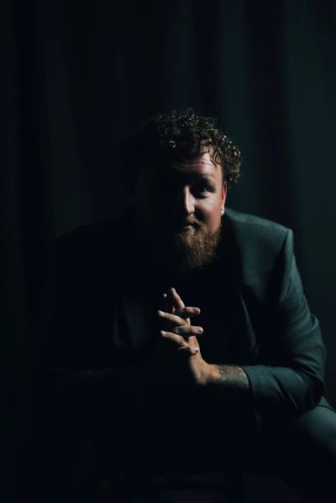 Portrait of a man with curly hair and beard in low light.