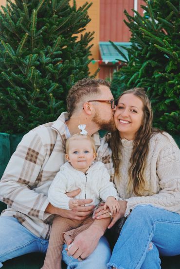 Family portrait with dad kissing mom and baby sitting in front.