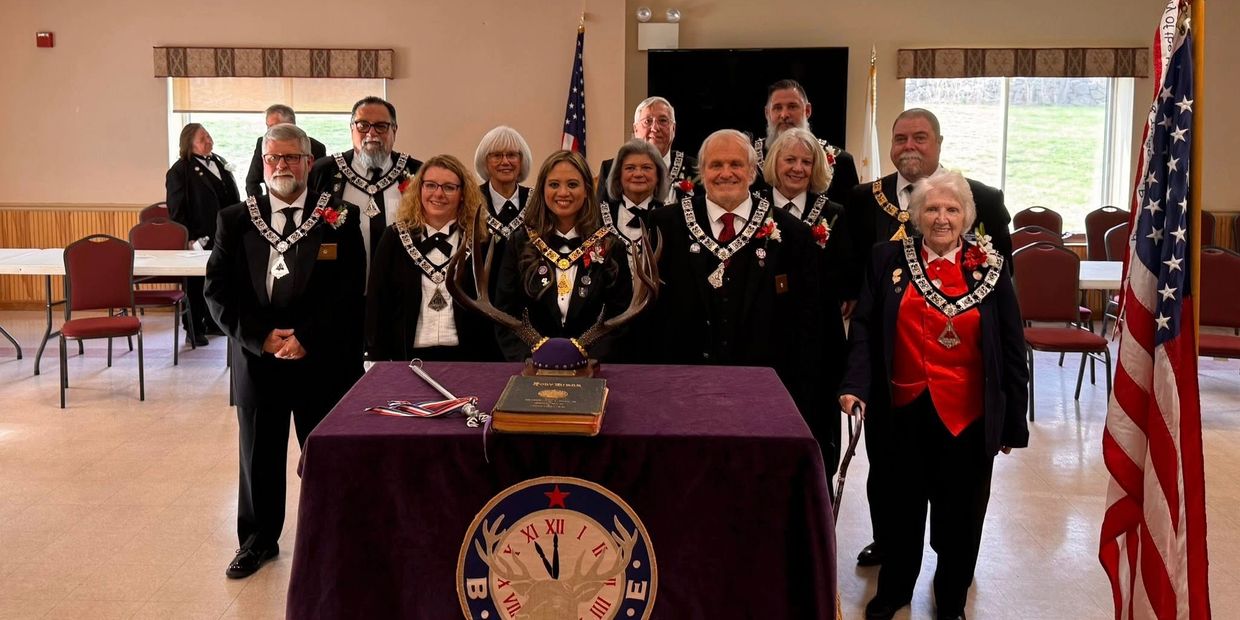 Group of formally dressed people posing behind a table with antlers and a book.
