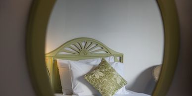 Reflection of a bed with green headboard and patterned pillow.