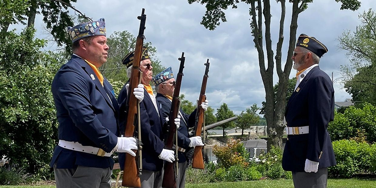 Veterans in uniform perform a ceremonial rifle salute outdoors.