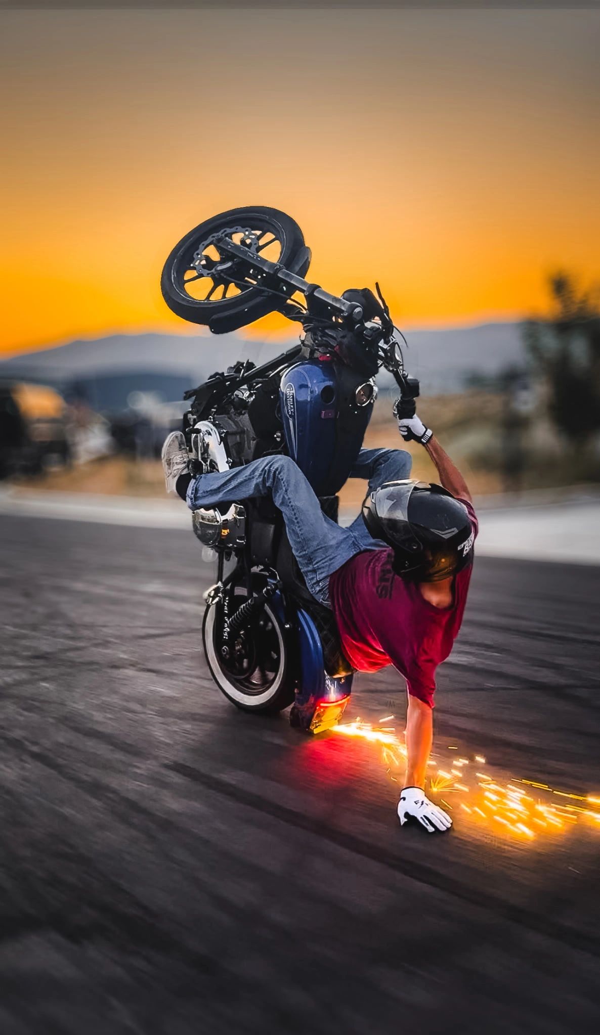 Motorcyclist performing a daring wheelie at sunset, sparks flying from the ground.