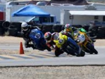 Four motorcyclists racing closely on a track, leaning into a turn.