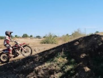 A person on a dirt bike preparing to ride up a dirt hill under a clear blue sky.