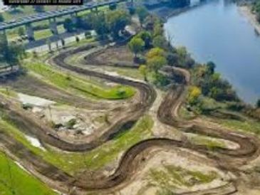 Aerial view of a winding dirt motocross track near a river and bridge.