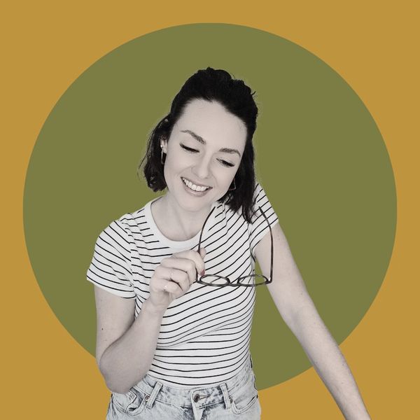 Kayley in black and white image, with a striped top, holding glasses and looking downwards whilst sm