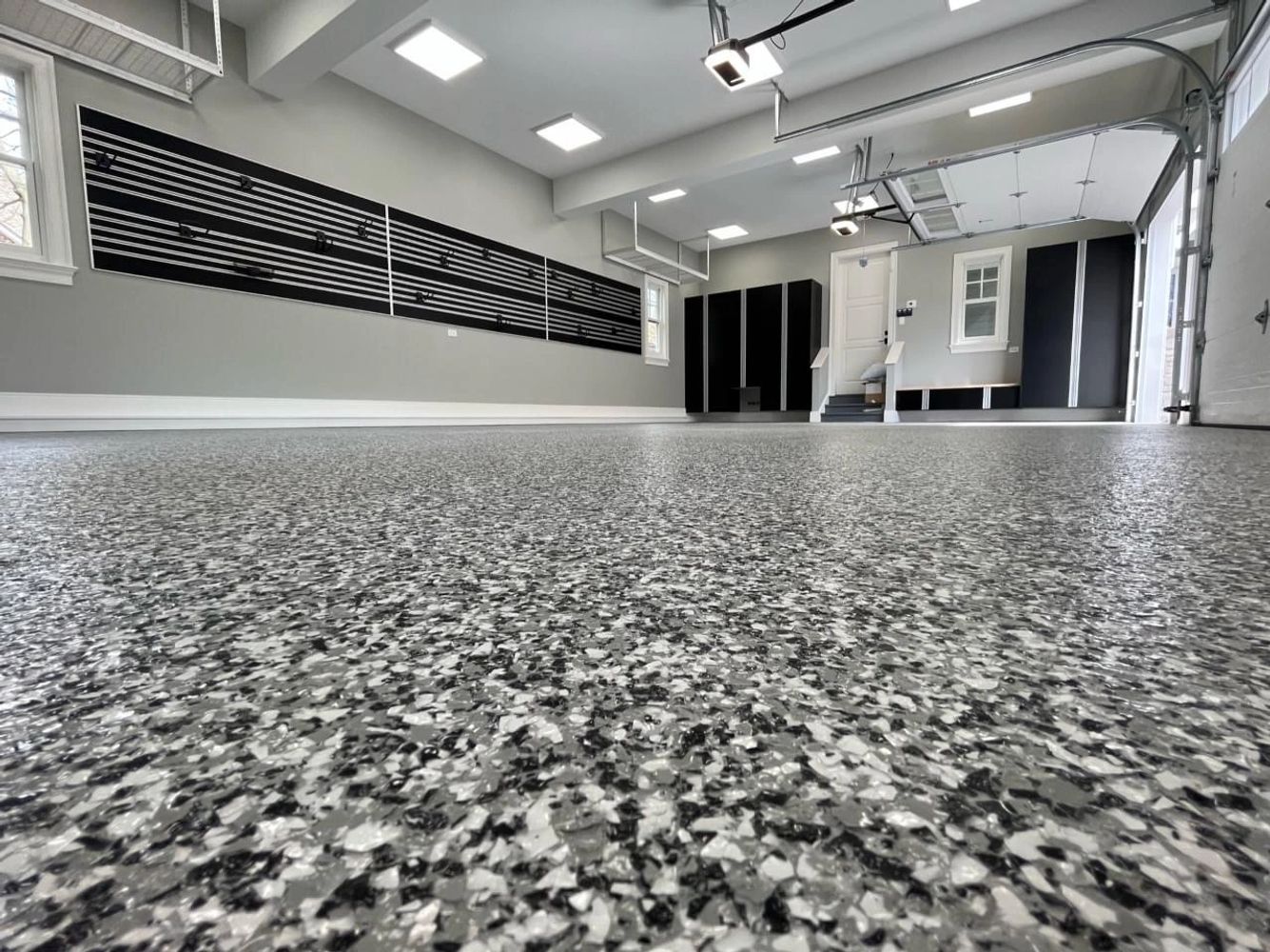 Clean, organized garage with speckled epoxy floor and black storage cabinets.