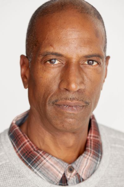 Close-up portrait of a serious middle-aged man in a plaid shirt and sweater.