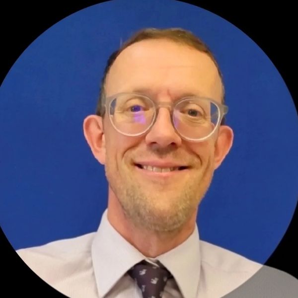 Smiling man in glasses and tie against a blue background.