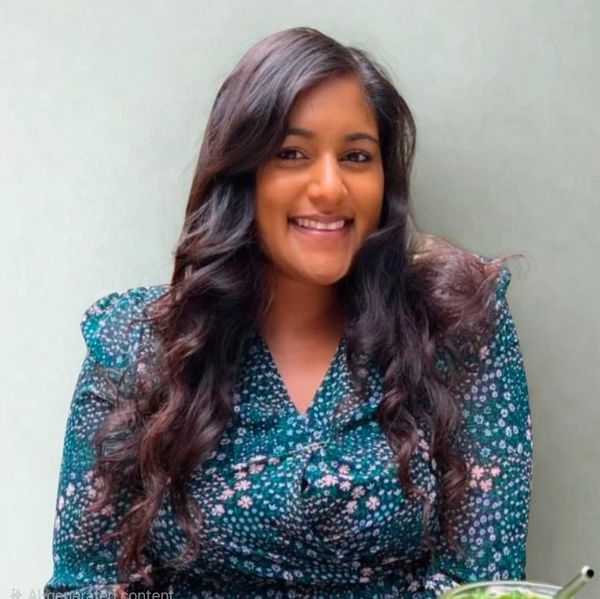 Smiling woman with long curly hair in a floral dress against a plain background.